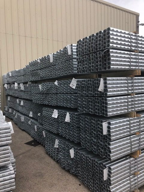 Image of steel metal trellising posts stacked horizontally in bundles in front of a warehouse.